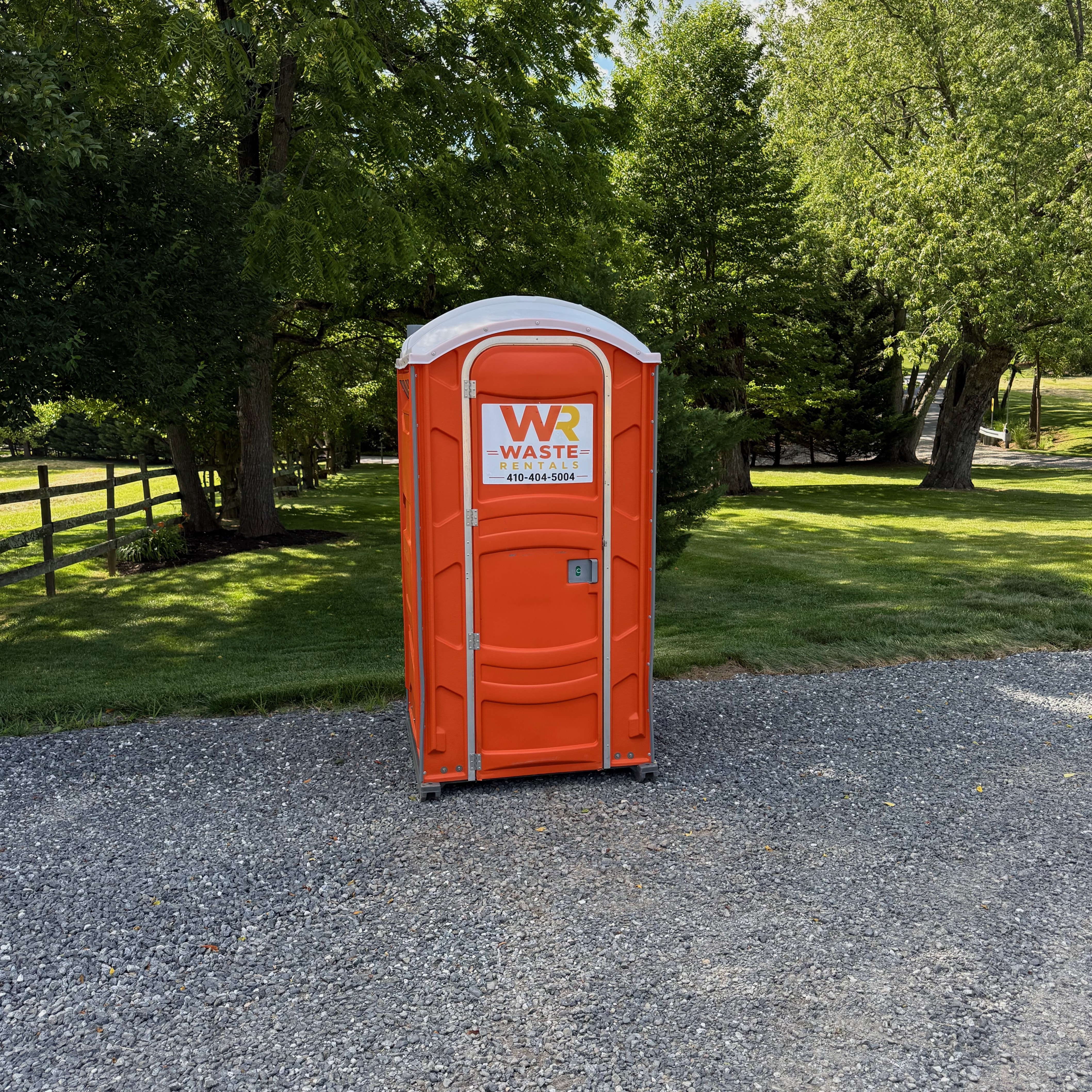 Orange Waste Rentals portable restroom in a green outdoor venue setting